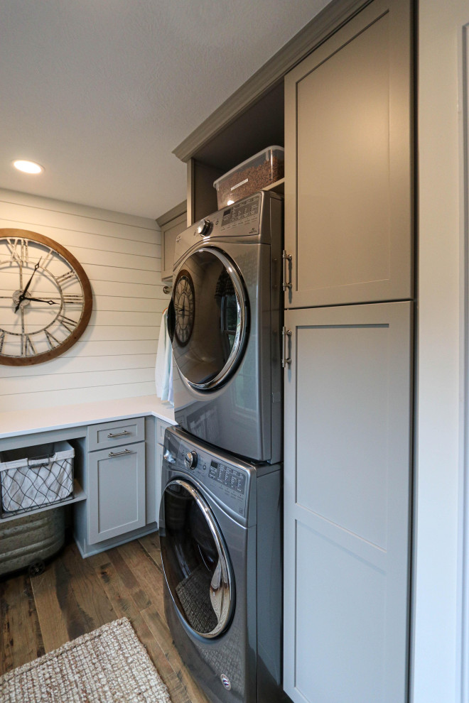 Inspiration for a small transitional u-shaped dedicated laundry room in Cleveland with recessed-panel cabinets, grey cabinets, quartz benchtops, white splashback, shiplap splashback, grey walls, a stacked washer and dryer and white benchtop.