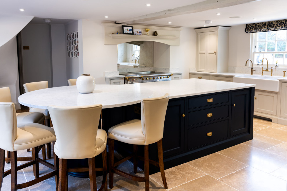 Design ideas for a large country cream and black l-shaped open plan kitchen in Essex with a belfast sink, shaker cabinets, black cabinets, quartz worktops, metallic splashback, glass sheet splashback, stainless steel appliances, limestone flooring, an island, beige floors, white worktops and a chimney breast.