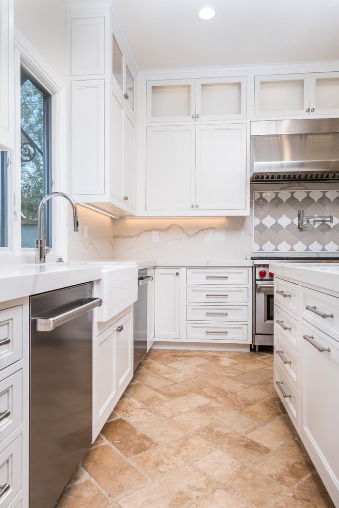 Mid-sized transitional l-shaped porcelain tile and beige floor enclosed kitchen photo in Orange County with a farmhouse sink, recessed-panel cabinets, white cabinets, quartz countertops, white backsplash, marble backsplash, stainless steel appliances and an island