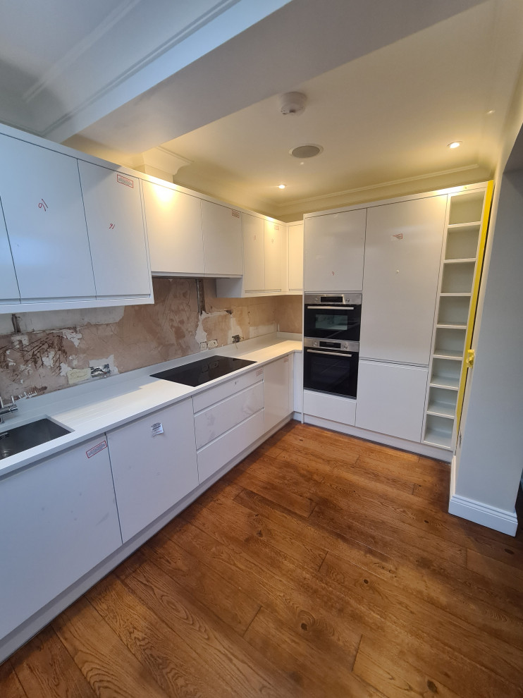Inspiration for a mid-sized modern l-shaped eat-in kitchen in London with an integrated sink, quartzite benchtops, light hardwood floors, white benchtop, flat-panel cabinets, white cabinets, porcelain splashback and panelled appliances.