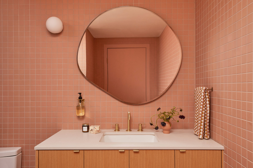 This is an example of a small retro bathroom in San Francisco with light wood cabinets, a built-in shower, a one-piece toilet, pink tiles, ceramic tiles, pink walls, ceramic flooring, a submerged sink, engineered stone worktops, pink floors, a hinged door, grey worktops, a wall niche, a single sink and a floating vanity unit.