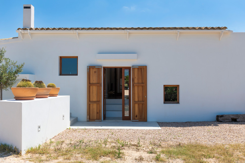 Cette photo montre une façade de maison blanche méditerranéenne en panneau de béton fibré de taille moyenne et de plain-pied avec un toit à deux pans, un toit en tuile et un toit marron.