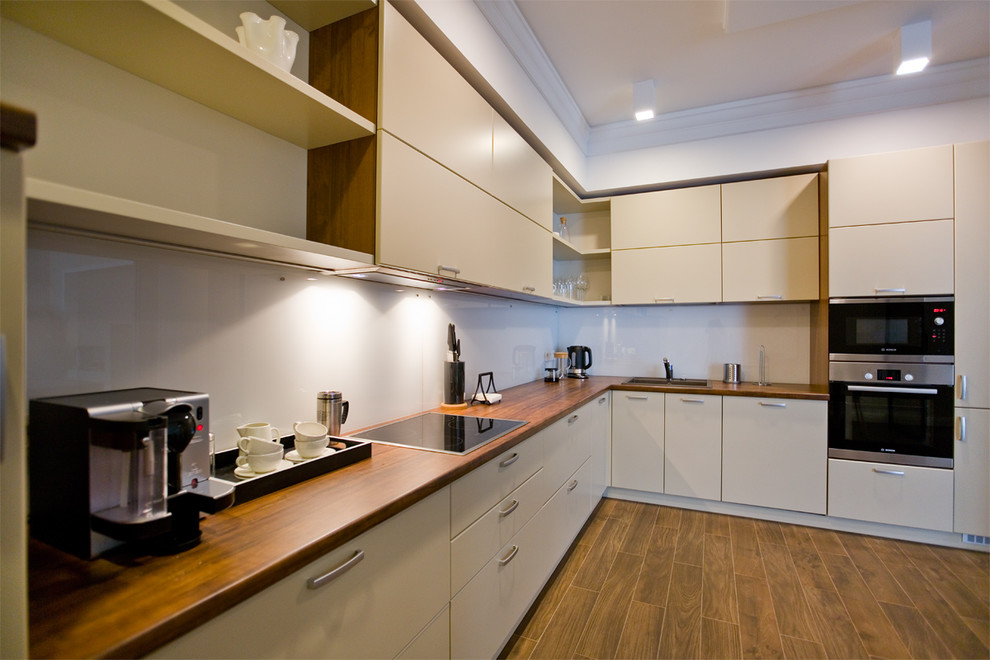 Mid-sized contemporary l-shaped eat-in kitchen in Saint Petersburg with a drop-in sink, flat-panel cabinets, beige cabinets, laminate benchtops, white splashback, glass tile splashback and porcelain floors.