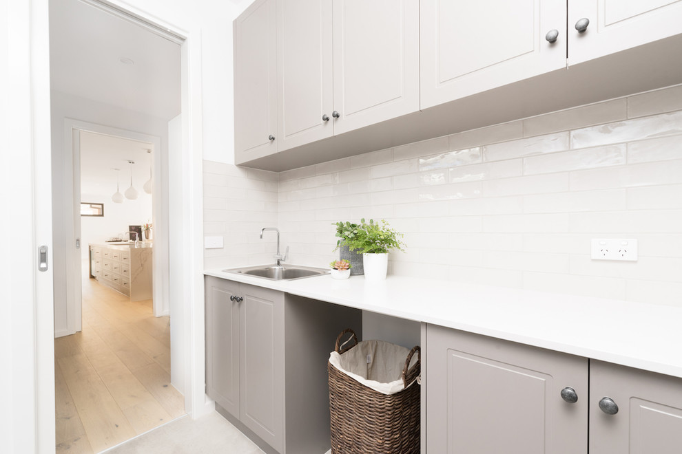 Photo of a mid-sized contemporary galley utility room in Melbourne with a single-bowl sink, white walls and white benchtop.