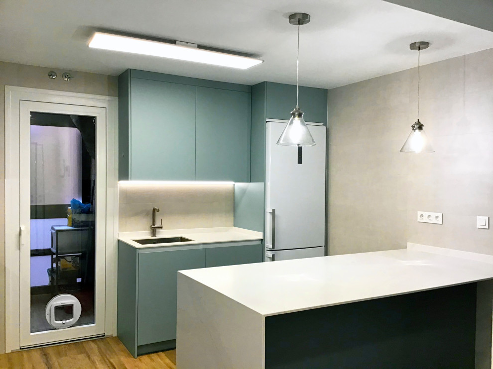 Example of a large minimalist u-shaped laminate floor and beige floor open concept kitchen design in Madrid with an integrated sink, green cabinets, solid surface countertops, white backsplash, white appliances, an island and white countertops