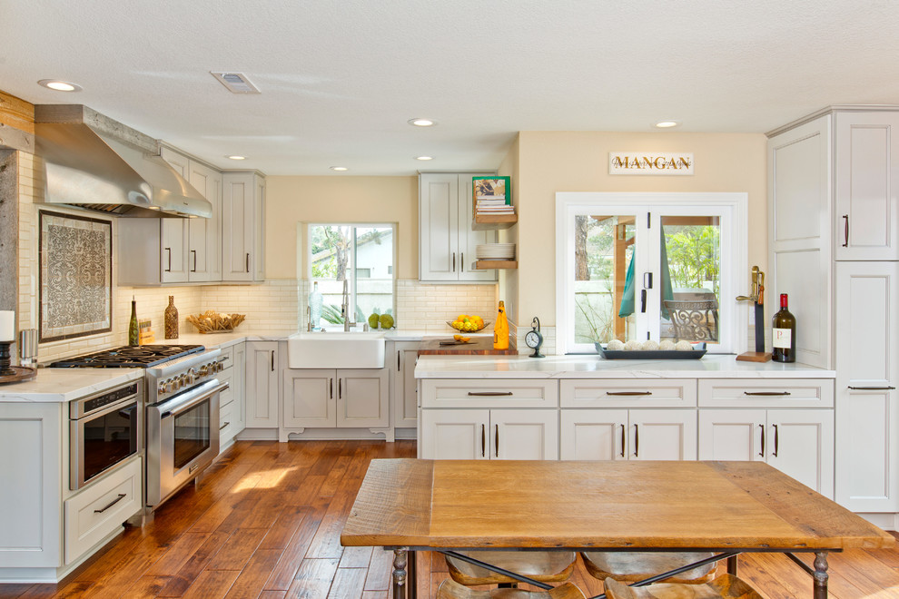 Inspiration for a mid-sized transitional u-shaped open plan kitchen in Tampa with a farmhouse sink, recessed-panel cabinets, grey cabinets, quartzite benchtops, beige splashback, porcelain splashback, stainless steel appliances, medium hardwood floors and no island.
