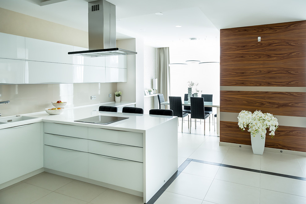 This is an example of a mid-sized contemporary l-shaped open plan kitchen in Novosibirsk with a drop-in sink, flat-panel cabinets, white cabinets, solid surface benchtops, beige splashback, porcelain splashback, black appliances, porcelain floors, a peninsula, beige floor and white benchtop.