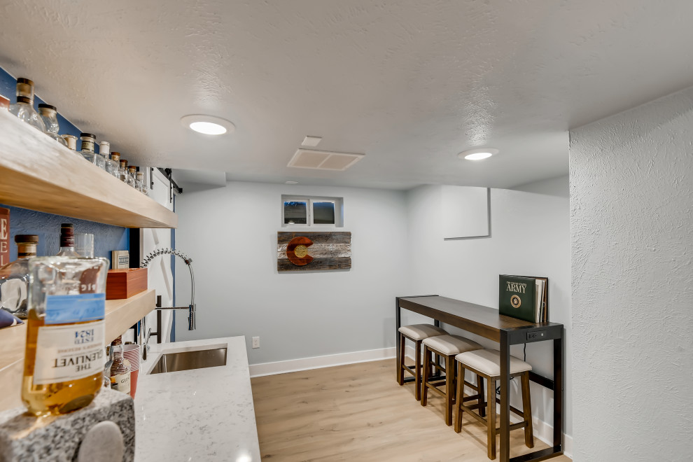 Cette photo montre un sous-sol tendance enterré et de taille moyenne avec un bar de salon, un mur bleu, un sol en vinyl, un sol marron et du papier peint.