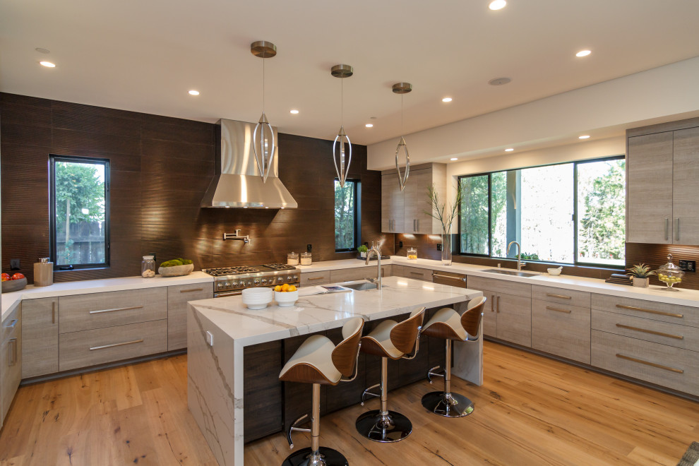 Large contemporary u-shaped open plan kitchen in Los Angeles with an undermount sink, flat-panel cabinets, grey cabinets, stainless steel appliances, brown floor, white benchtop, marble benchtops, brown splashback, porcelain splashback, light hardwood floors and with island.