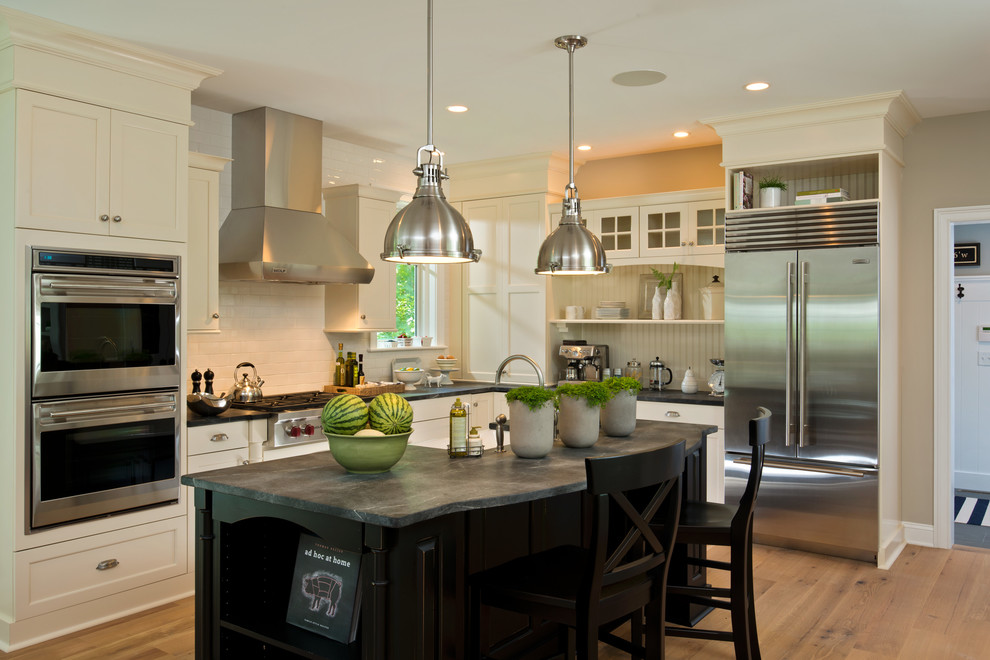 Example of a transitional l-shaped kitchen design in New York with a farmhouse sink, shaker cabinets, white cabinets, white backsplash, subway tile backsplash and stainless steel appliances
