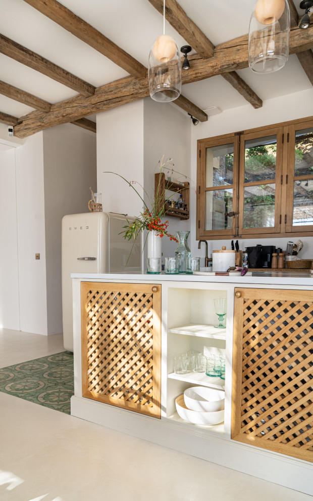 Cette image montre une cuisine américaine linéaire et beige et blanche méditerranéenne en bois clair de taille moyenne avec carreaux de ciment au sol, îlot, un sol vert, poutres apparentes et fenêtre au-dessus de l'évier.