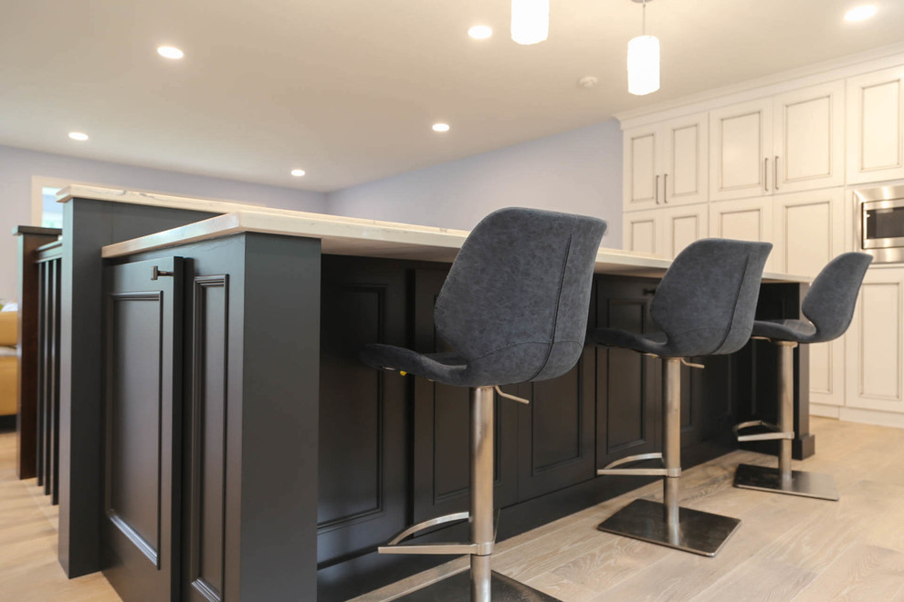 Eat-in kitchen - mid-sized transitional u-shaped light wood floor and beige floor eat-in kitchen idea with an undermount sink, recessed-panel cabinets, white cabinets, quartzite countertops, black backsplash, porcelain backsplash, stainless steel appliances, an island and white countertops