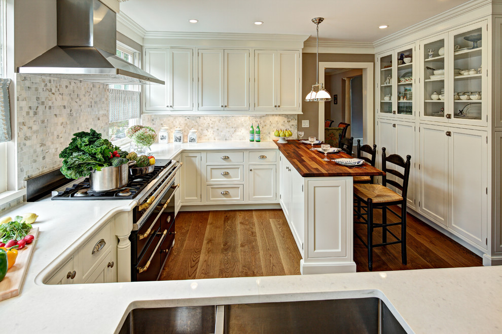 Photo of a traditional separate kitchen in New York with a double-bowl sink, shaker cabinets, beige cabinets, wood benchtops, beige splashback and black appliances.