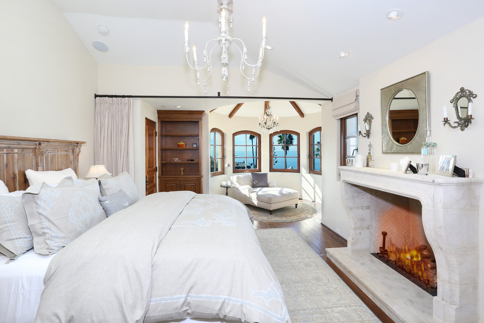 Tropical bedroom in Orange County with white walls, dark hardwood floors and a standard fireplace.