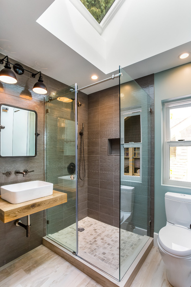 This is an example of a large contemporary master bathroom in Seattle with open cabinets, medium wood cabinets, an alcove tub, an alcove shower, a one-piece toilet, gray tile, porcelain tile, grey walls, porcelain floors, a vessel sink and wood benchtops.