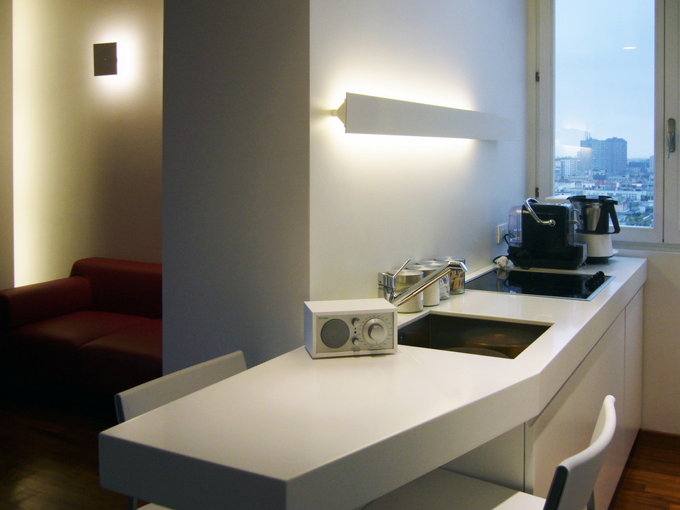 Photo of a small contemporary galley eat-in kitchen in Milan with an undermount sink, flat-panel cabinets, white cabinets, quartz benchtops, dark hardwood floors, a peninsula, brown floor and white benchtop.