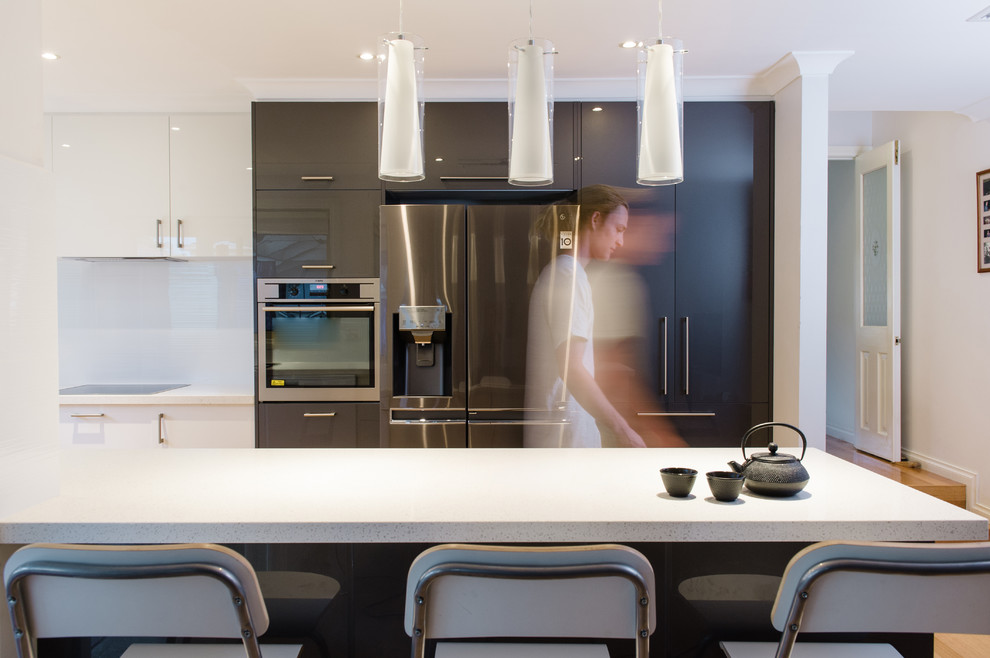 Mid-sized modern galley eat-in kitchen in Melbourne with open cabinets, white cabinets, solid surface benchtops, white splashback, glass tile splashback, stainless steel appliances, light hardwood floors, with island and beige floor.
