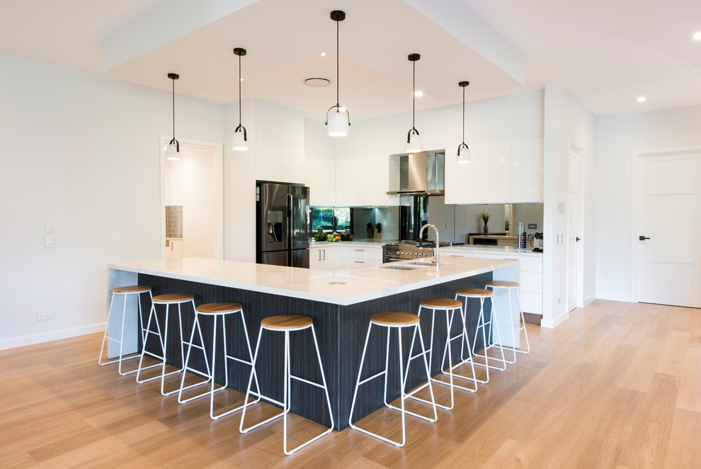 Mid-sized modern l-shaped kitchen in Brisbane with a double-bowl sink, flat-panel cabinets, white cabinets, quartz benchtops, mirror splashback, stainless steel appliances, light hardwood floors, brown floor, white benchtop and with island.