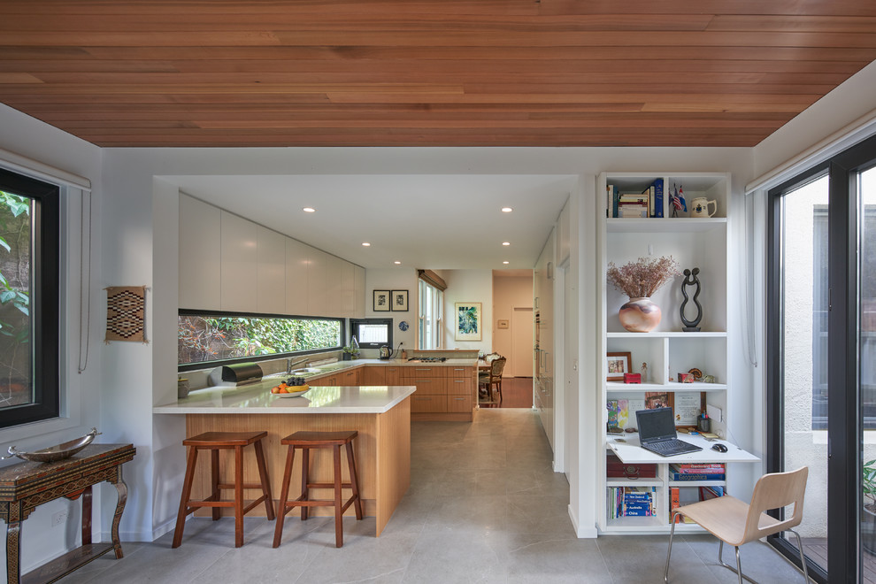 Photo of a mid-sized contemporary u-shaped kitchen in Melbourne with flat-panel cabinets, medium wood cabinets, window splashback, a peninsula, beige floor, a drop-in sink, panelled appliances and beige benchtop.
