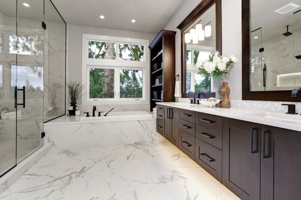 This is an example of a large contemporary master bathroom in Houston with shaker cabinets, brown cabinets, a drop-in tub, an alcove shower, grey walls, an undermount sink, multi-coloured floor, a hinged shower door and white benchtops.