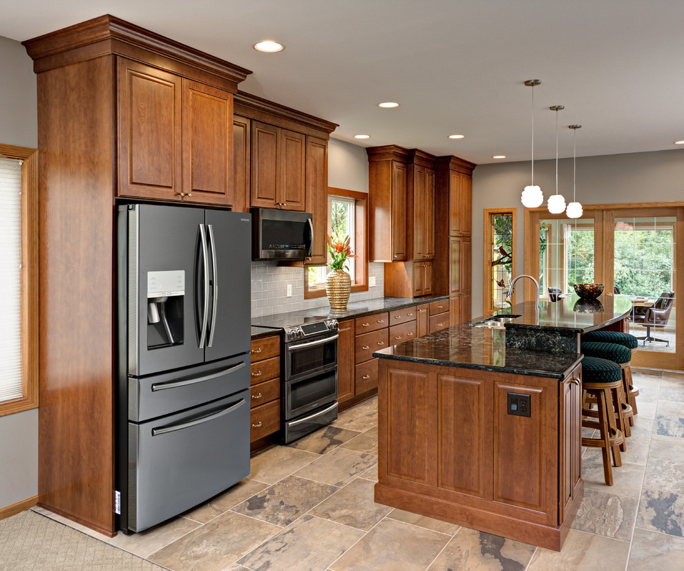 Photo of a large traditional galley eat-in kitchen in Minneapolis with a triple-bowl sink, raised-panel cabinets, medium wood cabinets, quartz benchtops, grey splashback, cement tile splashback, stainless steel appliances, porcelain floors, with island, grey floor and grey benchtop.