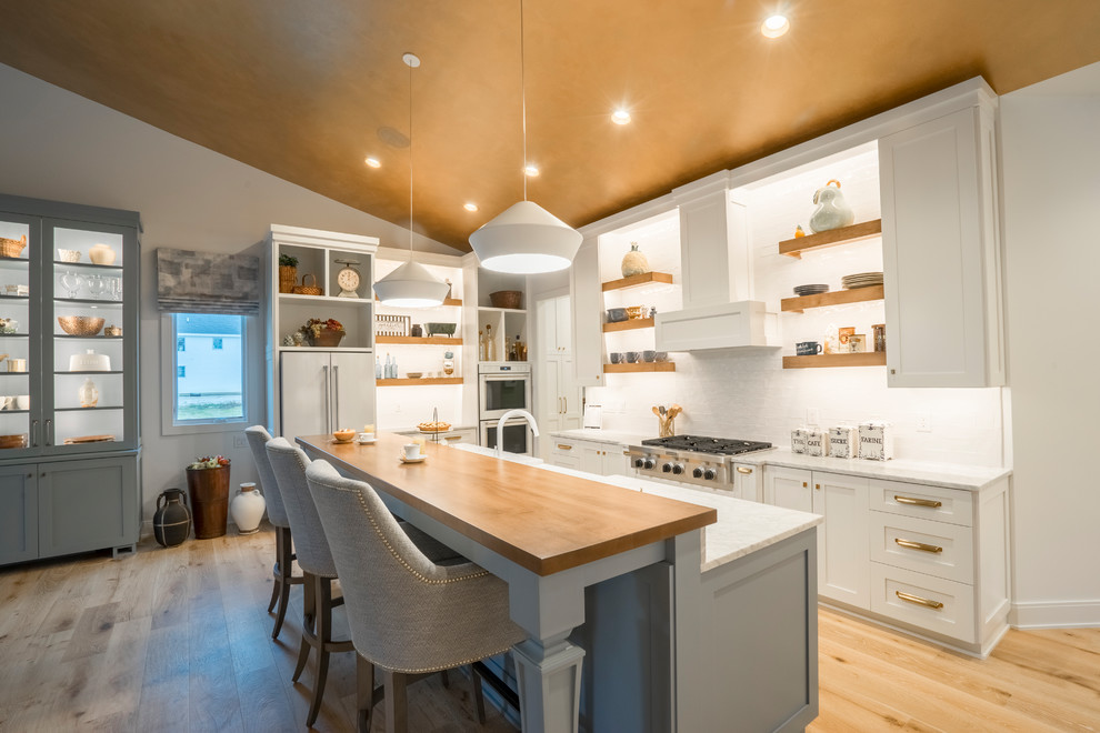 Design ideas for a large modern l-shaped open plan kitchen in Cleveland with a farmhouse sink, shaker cabinets, white cabinets, marble benchtops, white splashback, stainless steel appliances, light hardwood floors, with island, beige floor and white benchtop.
