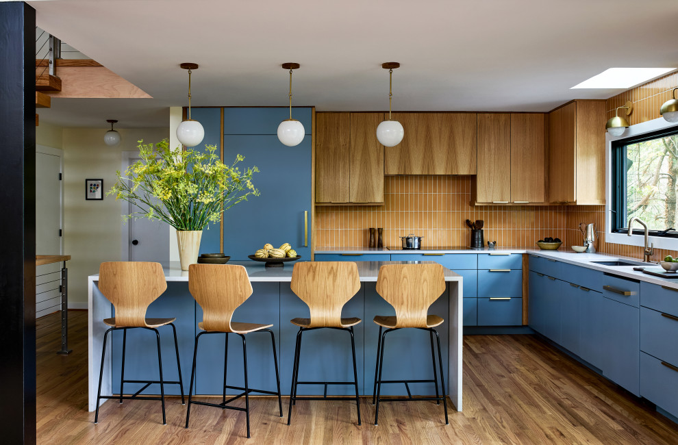 Example of a 1960s u-shaped medium tone wood floor and brown floor kitchen design in DC Metro with an undermount sink, flat-panel cabinets, blue cabinets, orange backsplash, paneled appliances, an island and white countertops