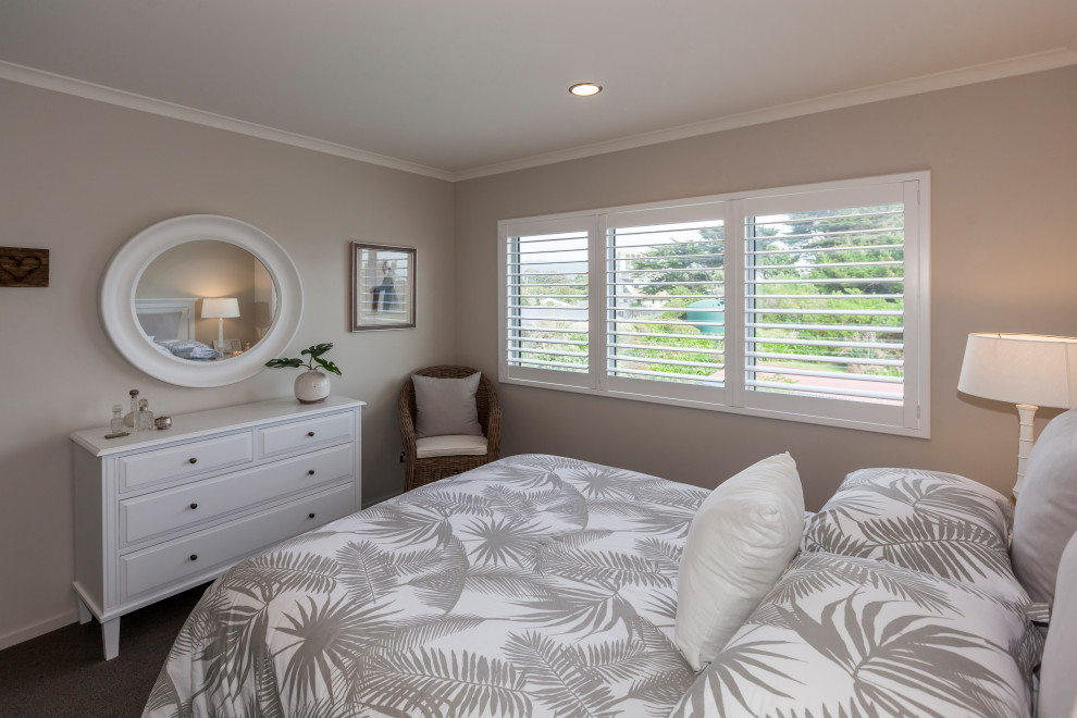 This is an example of a large beach style guest bedroom in Wellington with beige walls, carpet, brown floor and no fireplace.