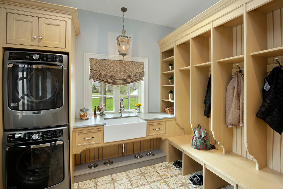 This is an example of a traditional utility room in Chicago with a farmhouse sink, recessed-panel cabinets, grey walls, ceramic floors, a stacked washer and dryer and light wood cabinets.