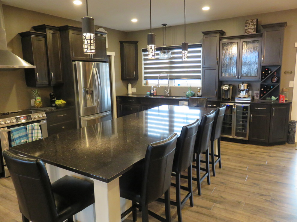 Example of a large transitional l-shaped light wood floor open concept kitchen design with gray cabinets, quartz countertops, stainless steel appliances, an island, a triple-bowl sink and shaker cabinets