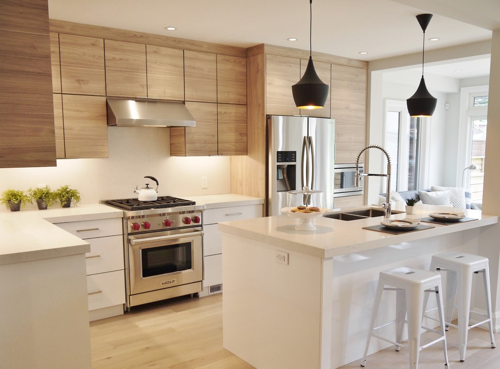 Photo of a small contemporary l-shaped open plan kitchen in Toronto with flat-panel cabinets, white splashback, stainless steel appliances, light hardwood floors, with island, light wood cabinets and an undermount sink.