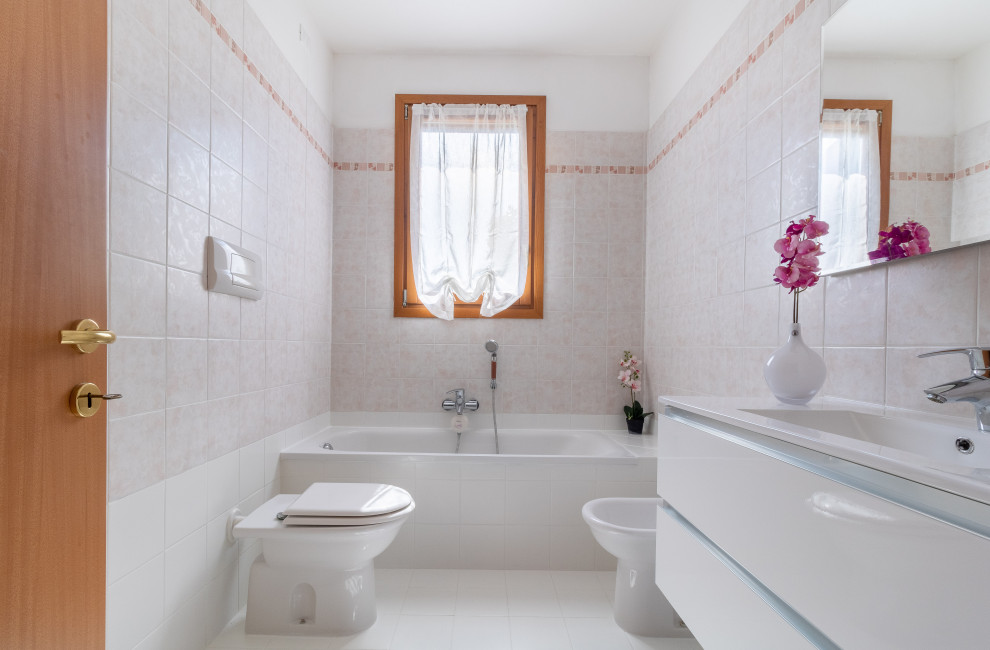 Exempel på ett modernt vit vitt badrum, med släta luckor, vita skåp, ett undermonterat badkar, en bidé, grå kakel, vita väggar, ett integrerad handfat och vitt golv
