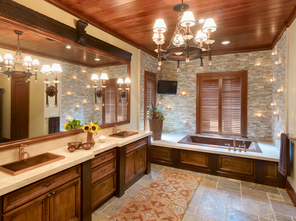 This is an example of a traditional bathroom with a drop-in sink, recessed-panel cabinets, dark wood cabinets, a drop-in tub, gray tile and stone tile.