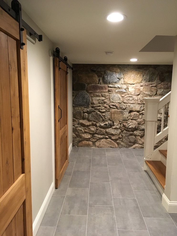 This is an example of a large country look-out basement in New York with grey walls, porcelain floors, no fireplace and grey floor.