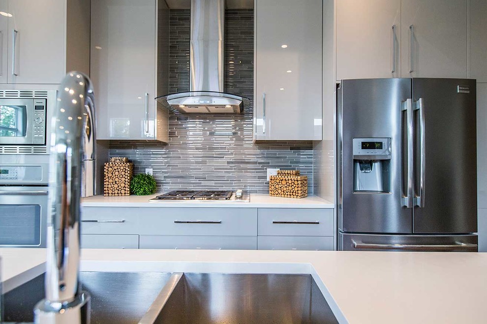Mid-sized contemporary single-wall open plan kitchen in Calgary with a double-bowl sink, flat-panel cabinets, beige cabinets, solid surface benchtops, beige splashback, matchstick tile splashback, stainless steel appliances, medium hardwood floors and with island.