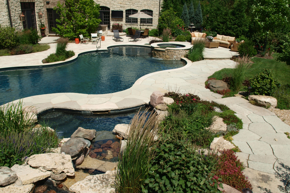 This is an example of a large arts and crafts backyard custom-shaped natural pool in Chicago with a water feature and natural stone pavers.