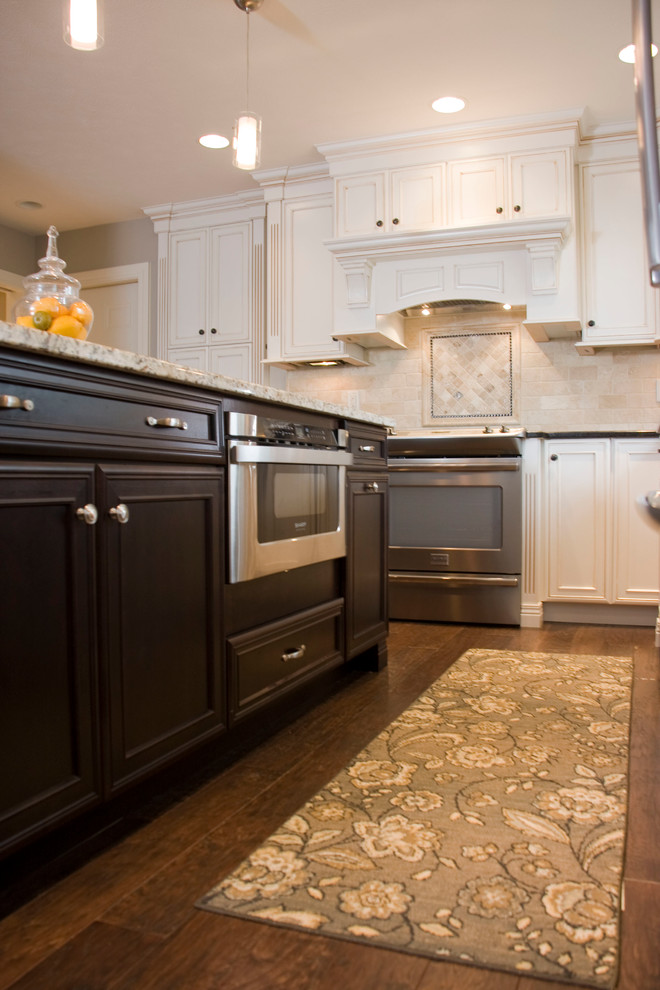 Inspiration for a large transitional u-shaped medium tone wood floor kitchen remodel in Cincinnati with an undermount sink, recessed-panel cabinets, white cabinets, granite countertops, beige backsplash, stone tile backsplash, stainless steel appliances and an island