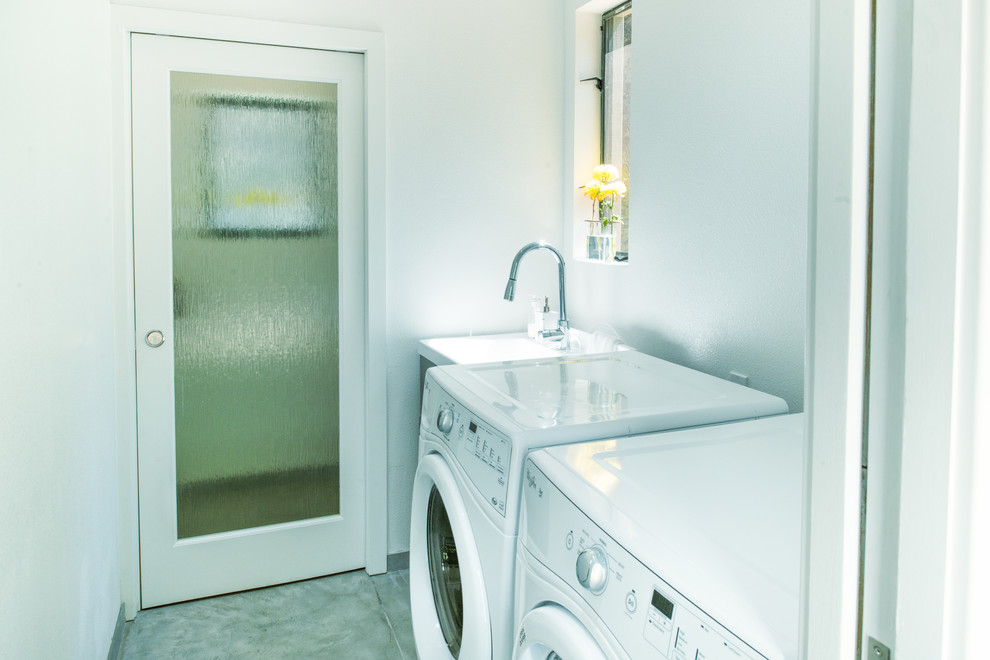 This is an example of a small modern galley dedicated laundry room in San Francisco with an utility sink, white walls, concrete floors and a side-by-side washer and dryer.