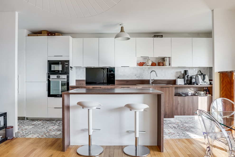 This is an example of a large single-wall eat-in kitchen in Paris with white cabinets, wood benchtops, stainless steel appliances, with island, brown benchtop, white splashback, mosaic tile splashback and cement tiles.