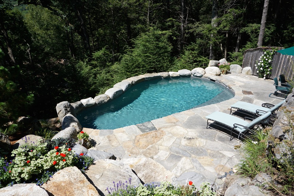 This is an example of a mid-sized country backyard custom-shaped natural pool in New York with natural stone pavers.