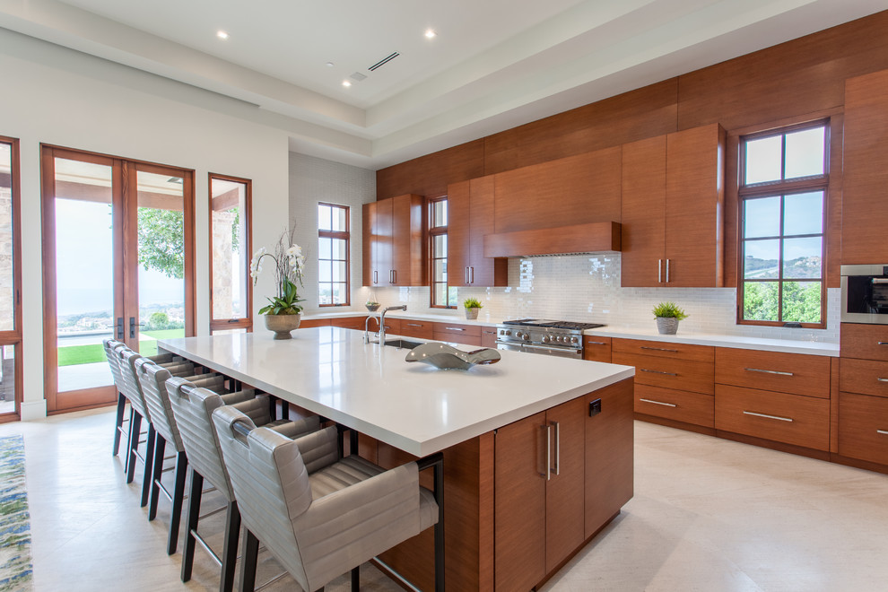 Design ideas for a mediterranean l-shaped kitchen in Orange County with an undermount sink, flat-panel cabinets, medium wood cabinets, white splashback, glass tile splashback, stainless steel appliances, with island and white floor.
