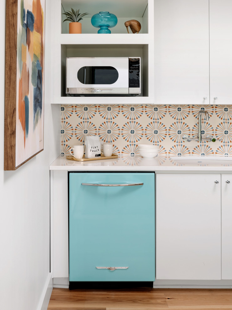 Small midcentury eat-in kitchen in Austin with a drop-in sink, flat-panel cabinets, white cabinets, quartz benchtops, white splashback, cement tile splashback, stainless steel appliances, medium hardwood floors, with island, beige floor, white benchtop and wood.
