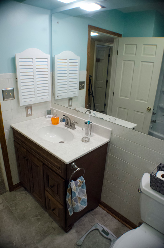 Example of a small transitional gray tile and ceramic tile porcelain tile alcove bathtub design in Chicago with raised-panel cabinets, dark wood cabinets, a two-piece toilet, blue walls, an integrated sink and marble countertops