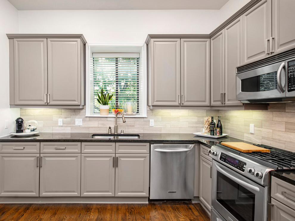 Mid-sized transitional l-shaped medium tone wood floor enclosed kitchen photo in Dallas with an undermount sink, raised-panel cabinets, granite countertops, subway tile backsplash, gray cabinets, gray backsplash, stainless steel appliances and black countertops