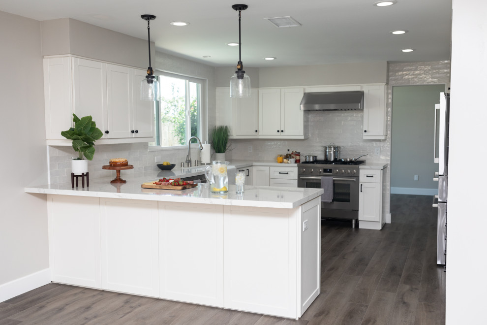 This is an example of a large country eat-in kitchen in San Diego with a farmhouse sink, shaker cabinets, white cabinets, quartzite benchtops, white splashback, subway tile splashback, stainless steel appliances, vinyl floors, a peninsula, grey floor and white benchtop.