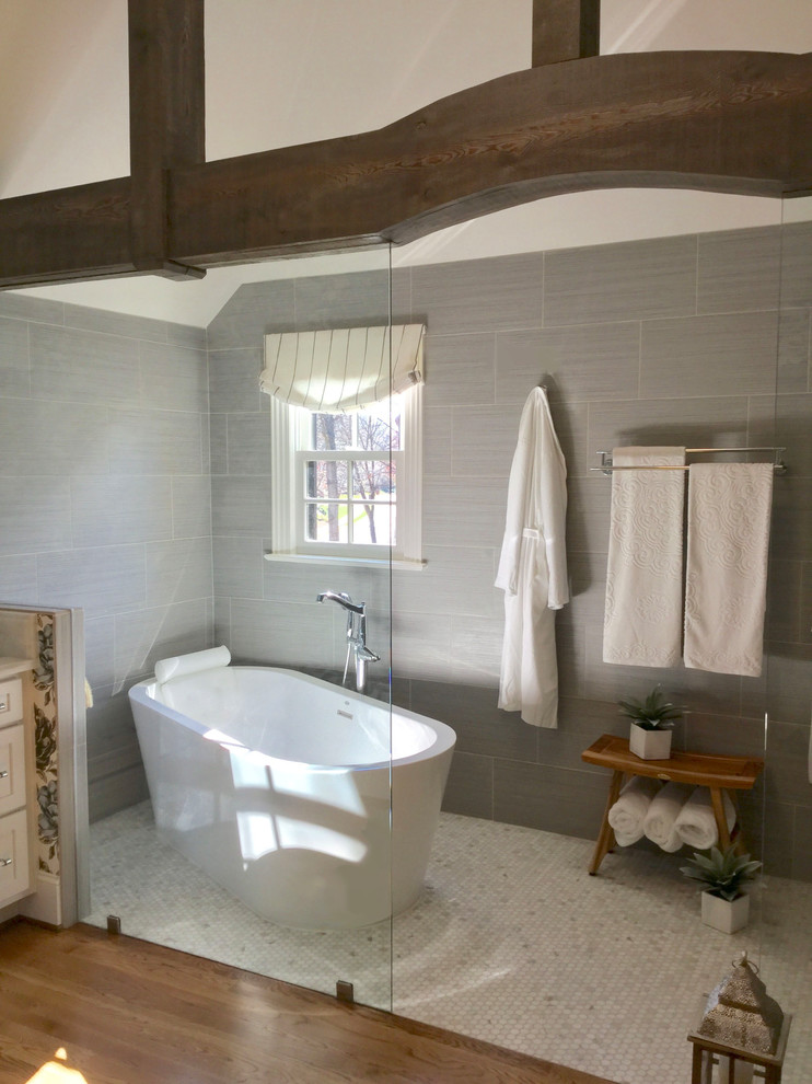Design ideas for a mid-sized transitional master wet room bathroom in Other with shaker cabinets, white cabinets, a freestanding tub, a one-piece toilet, gray tile, porcelain tile, white walls, an undermount sink, marble benchtops, medium hardwood floors and brown floor.