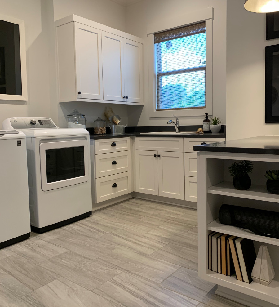 This is an example of an industrial dedicated laundry room in Charlotte with an utility sink, shaker cabinets, white cabinets, quartzite benchtops, white walls, ceramic floors, a side-by-side washer and dryer and black benchtop.