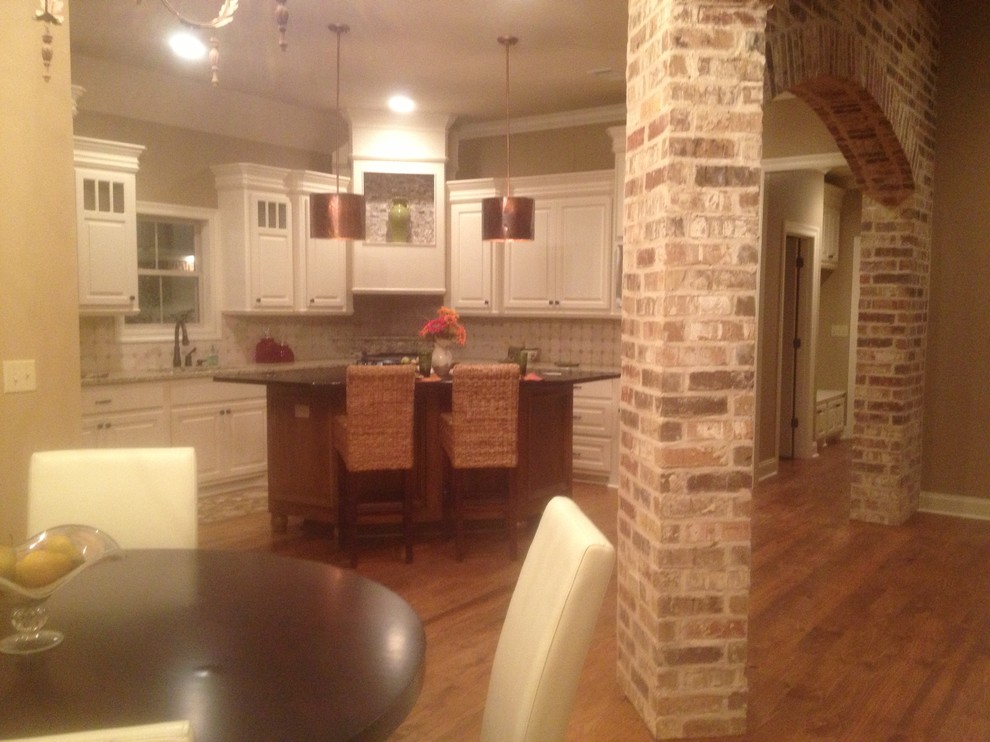 Inspiration for a mid-sized medium tone wood floor kitchen remodel with an undermount sink, glass-front cabinets, beige cabinets, granite countertops, beige backsplash, ceramic backsplash, stainless steel appliances and an island
