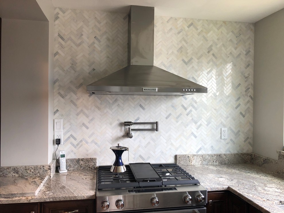 Mid-sized elegant l-shaped light wood floor and brown floor eat-in kitchen photo with an undermount sink, raised-panel cabinets, dark wood cabinets, granite countertops, multicolored backsplash, ceramic backsplash, stainless steel appliances, an island and multicolored countertops