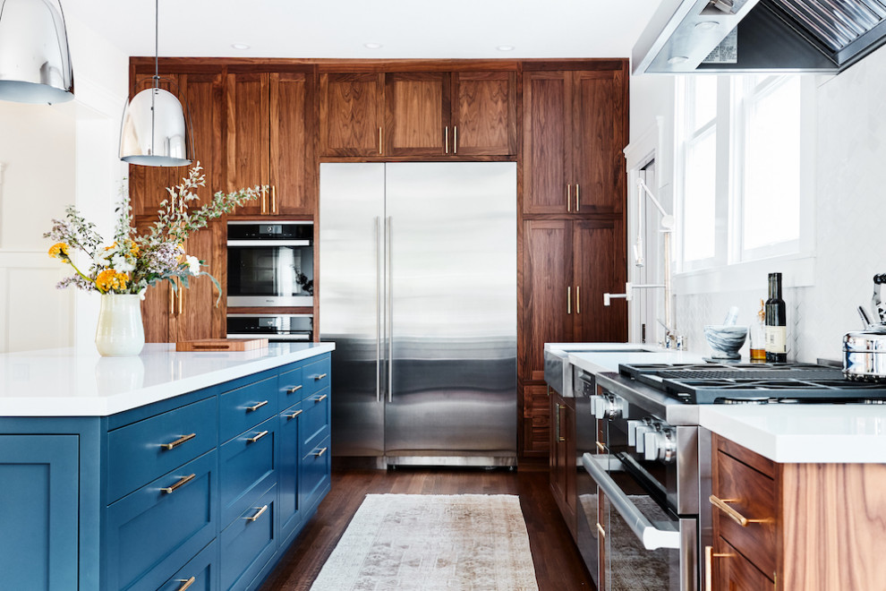 Photo of a contemporary l-shaped kitchen in San Francisco with a farmhouse sink, shaker cabinets, dark wood cabinets, stainless steel appliances, dark hardwood floors, with island, brown floor and white benchtop.